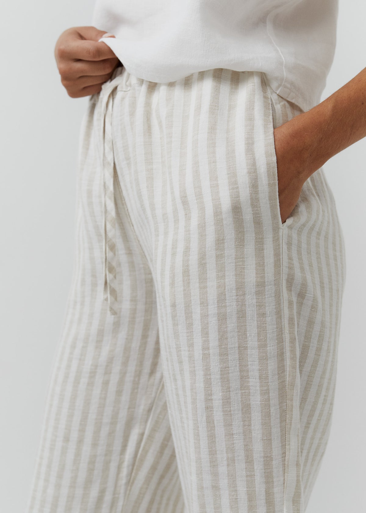 Close-up of beige linen trousers with an elastic drawstring waist and side pocket.