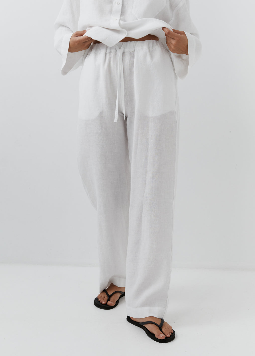 Close-up of an elasticated waist and drawstring on white linen trousers.