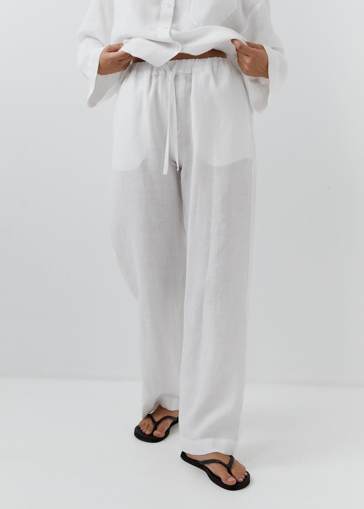 Close-up of an elasticated waist and drawstring on white linen trousers.